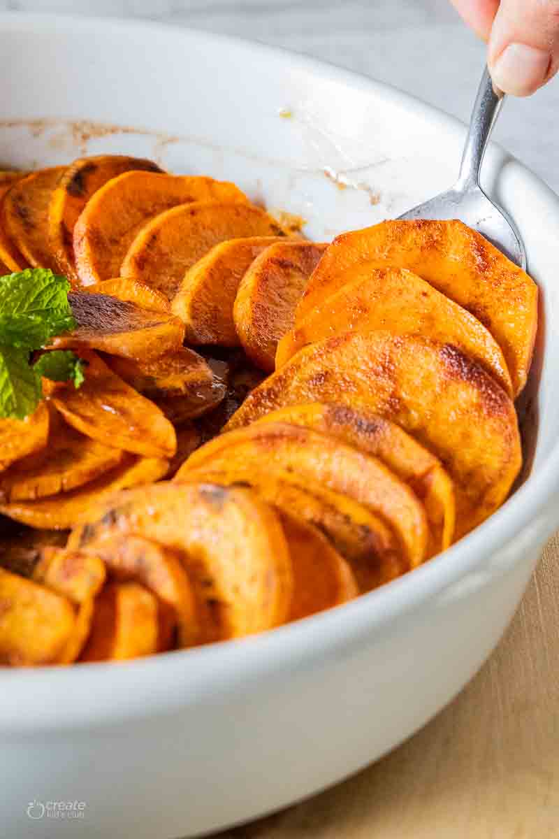 spoon scooping sweet potato slices out of baking dish