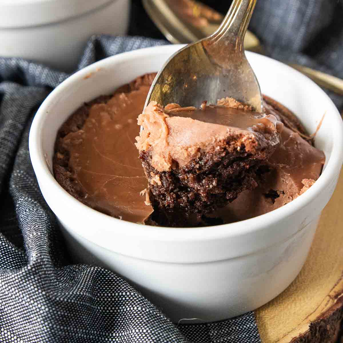 spoon scooping chocolate cake topped with icing from soufflé dish