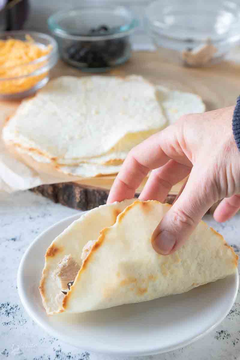 hand pinching tortilla filled with taco ingredients together