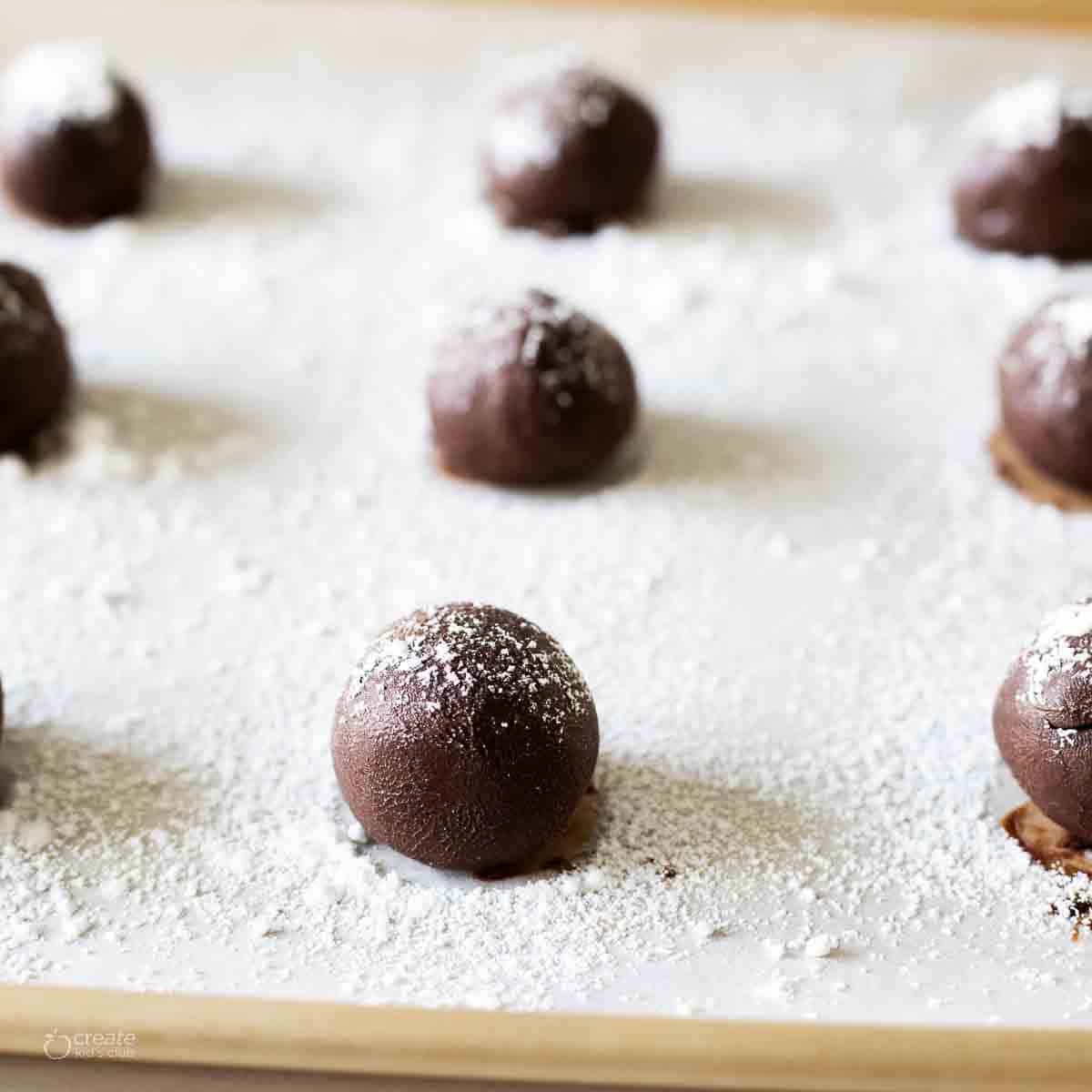 Rolled hot chocolate bombs on a tray dusted with powdered sugar.