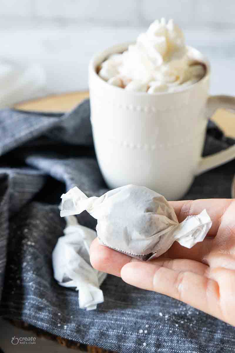 A hand holding a wax paper wrapped hot chocolate bomb.