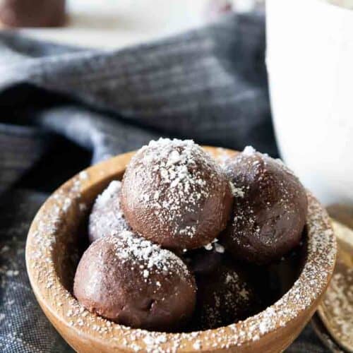 Hot chocolate bombs layered in a bowl next to a mug.