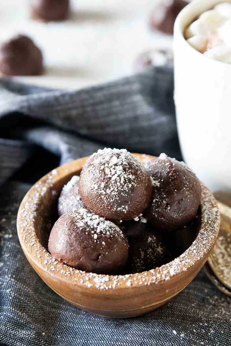 Hot chocolate bombs layered in a bowl next to a mug.