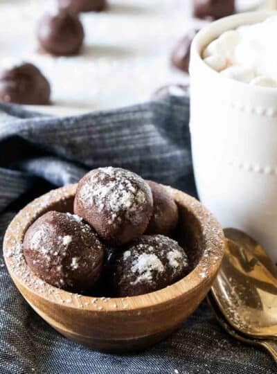 A square cropped photo of hot chocolate bombs in a bowl next to a mug.