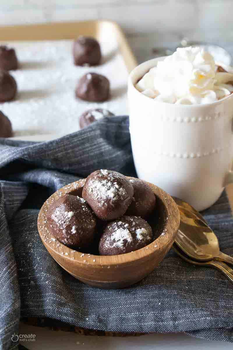 Hot chocolate bombs in a bowl next to a mug.