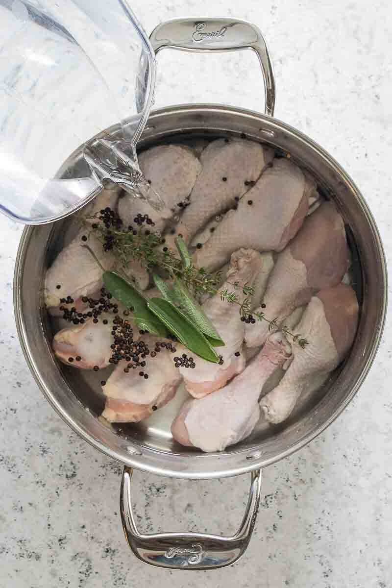 water poured into stock pot filled with chicken legs, spices and herbs