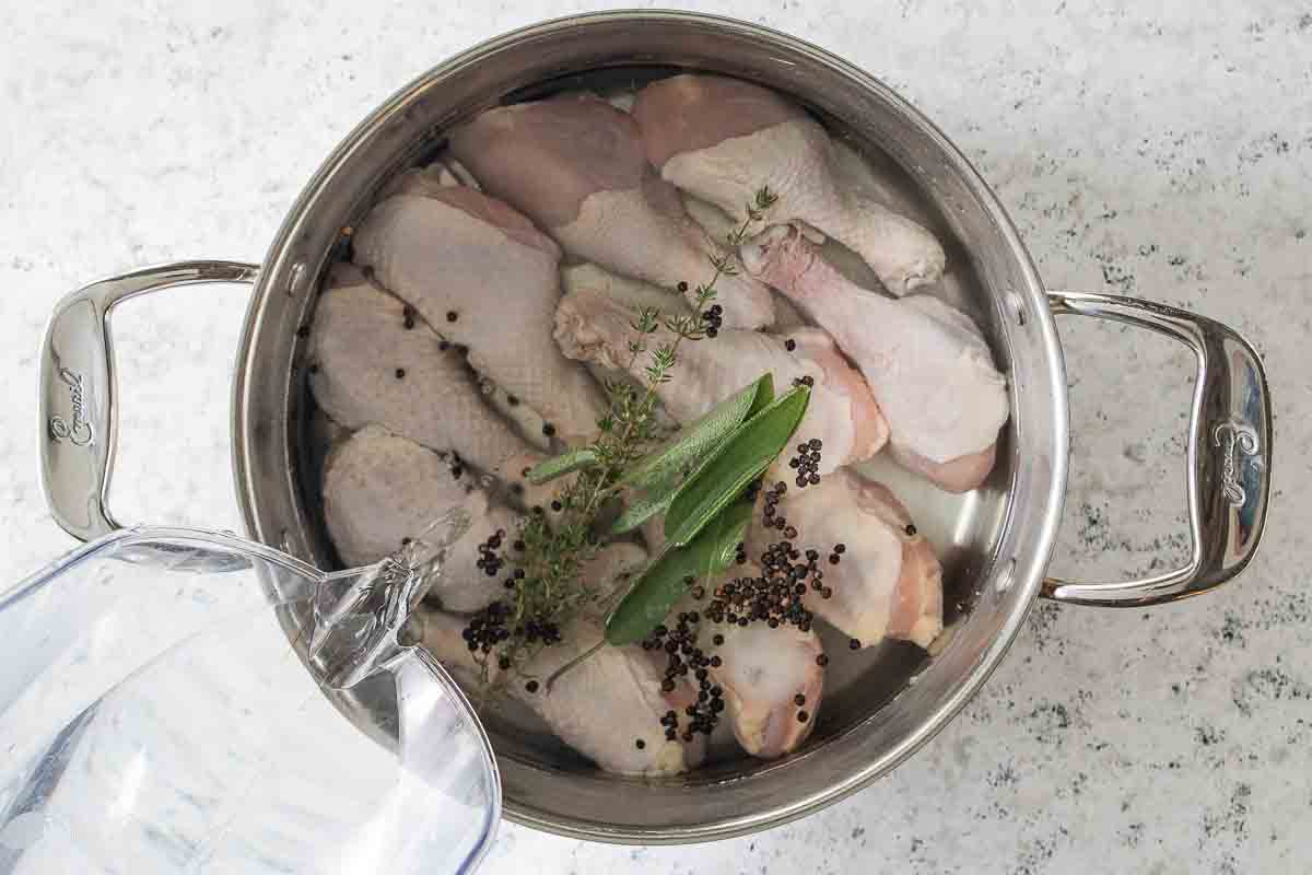 water poured into stock pot filled with chicken legs, spices and herbs