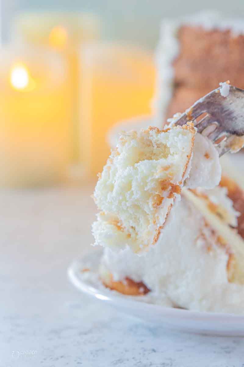 fork scooping a bite of iced white cake from plate