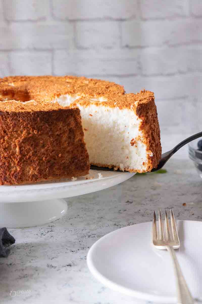 spatula removing slice of angel food cake from cake stand