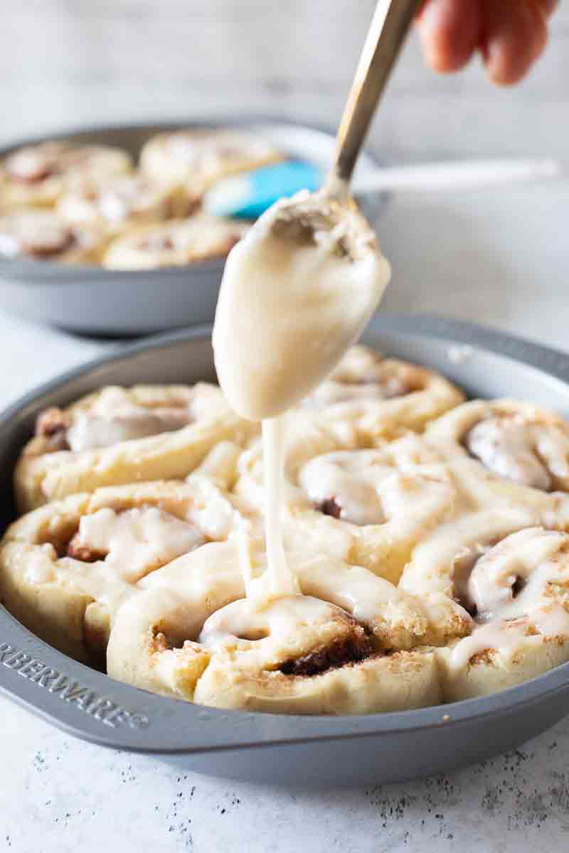 spoon drizzling icing on top of baked gluten-free cinnamon rolls