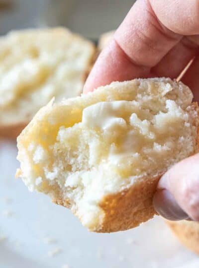 A hand holding a buttered gluten free dinner roll.