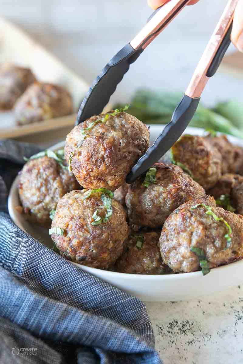 tongs picking up a gluten-free meatball from a large bowl