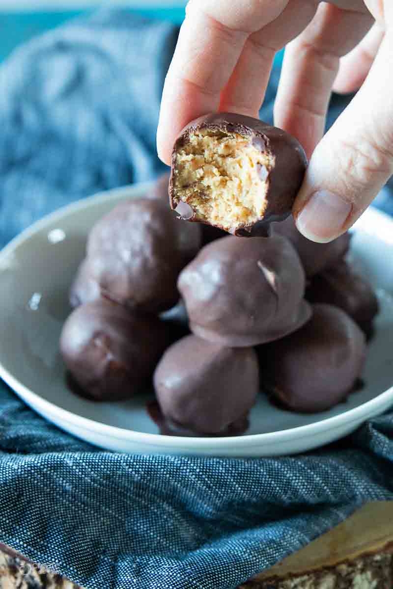 hand holding a peanut butter ball next to a bowl filled