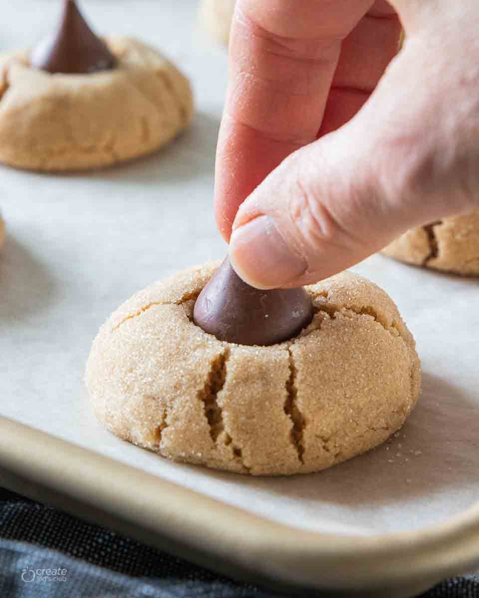 hand pressing chocolate kiss into peanut butter cookie