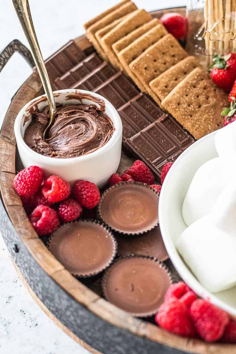 s'more charcuterie board filled with graham crackers, chocolate, raspberries, marshmallows and chocolate