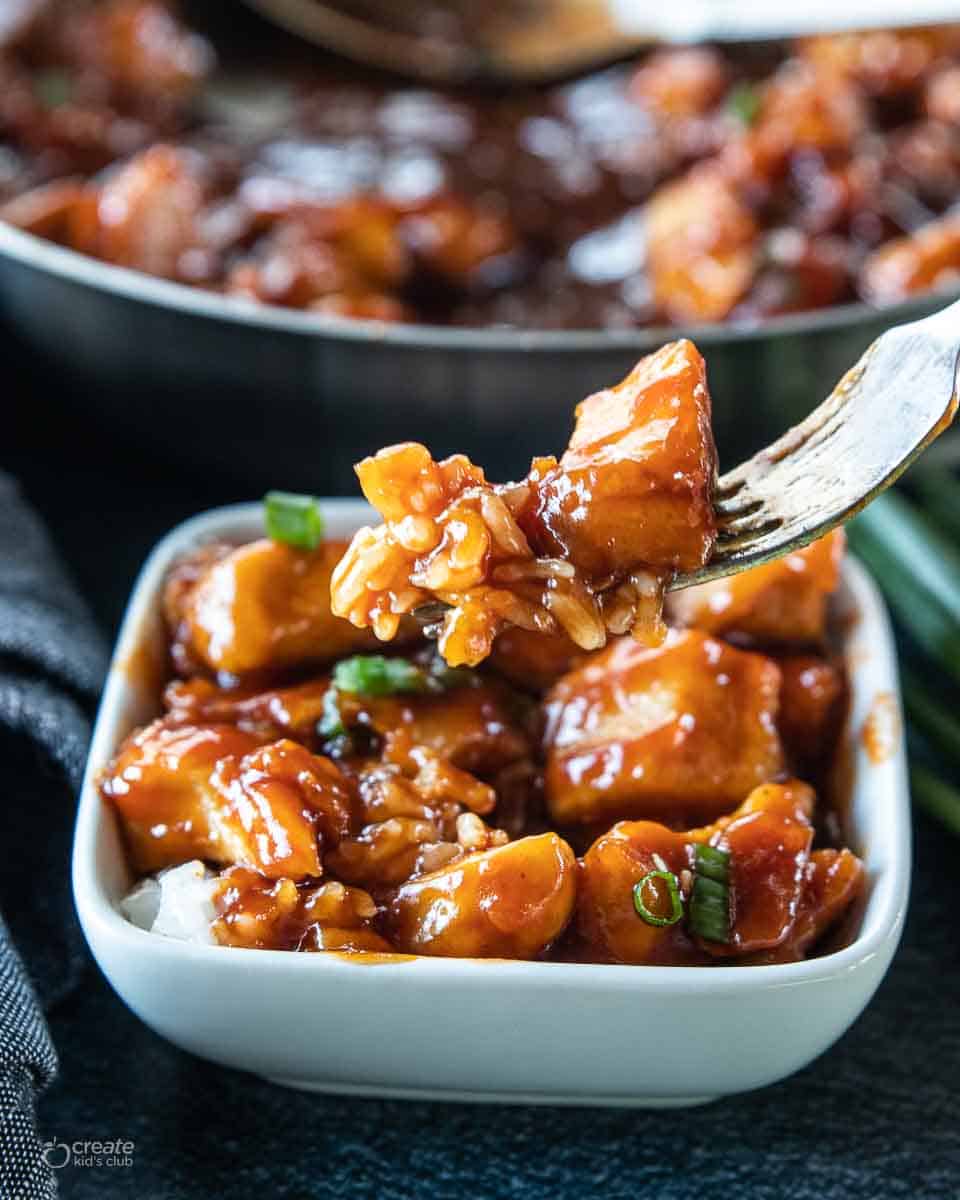 fork scooping sesame chicken from a bowl
