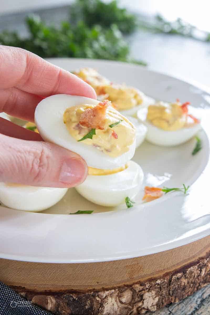 hand picking up a deviled egg from platter