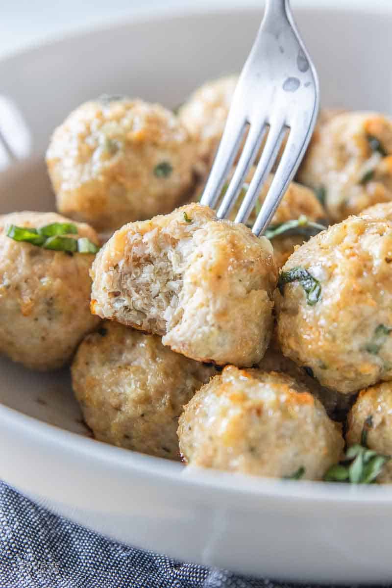 fork scooping a chicken meatball from a serving bowl