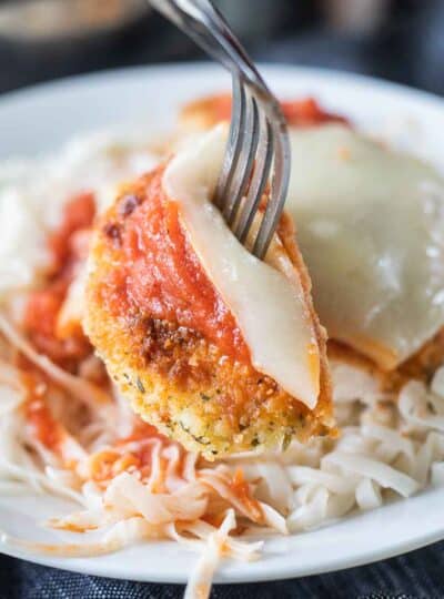 A close up of a sliced piece of a gluten free chicken parmesan coated in breading, sauce, and cheese.