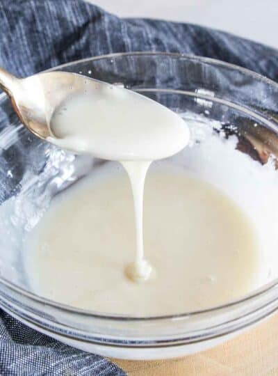 Gluten free icing spooned from a bowl in a square crop.