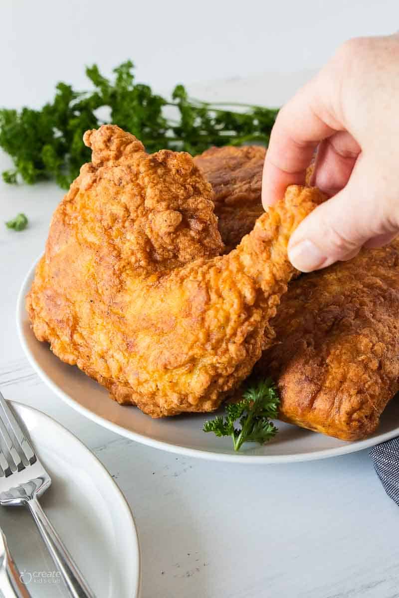 hand selecting a piece of fried chicken from plate