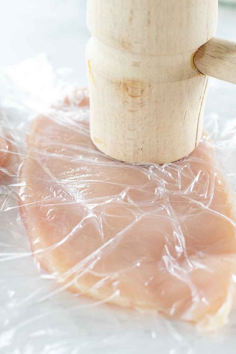 A thin chicken breast covered in plastic wrap with a mallet.