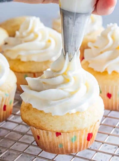 Gluten free frosting being piped onto a vanilla cupcake.