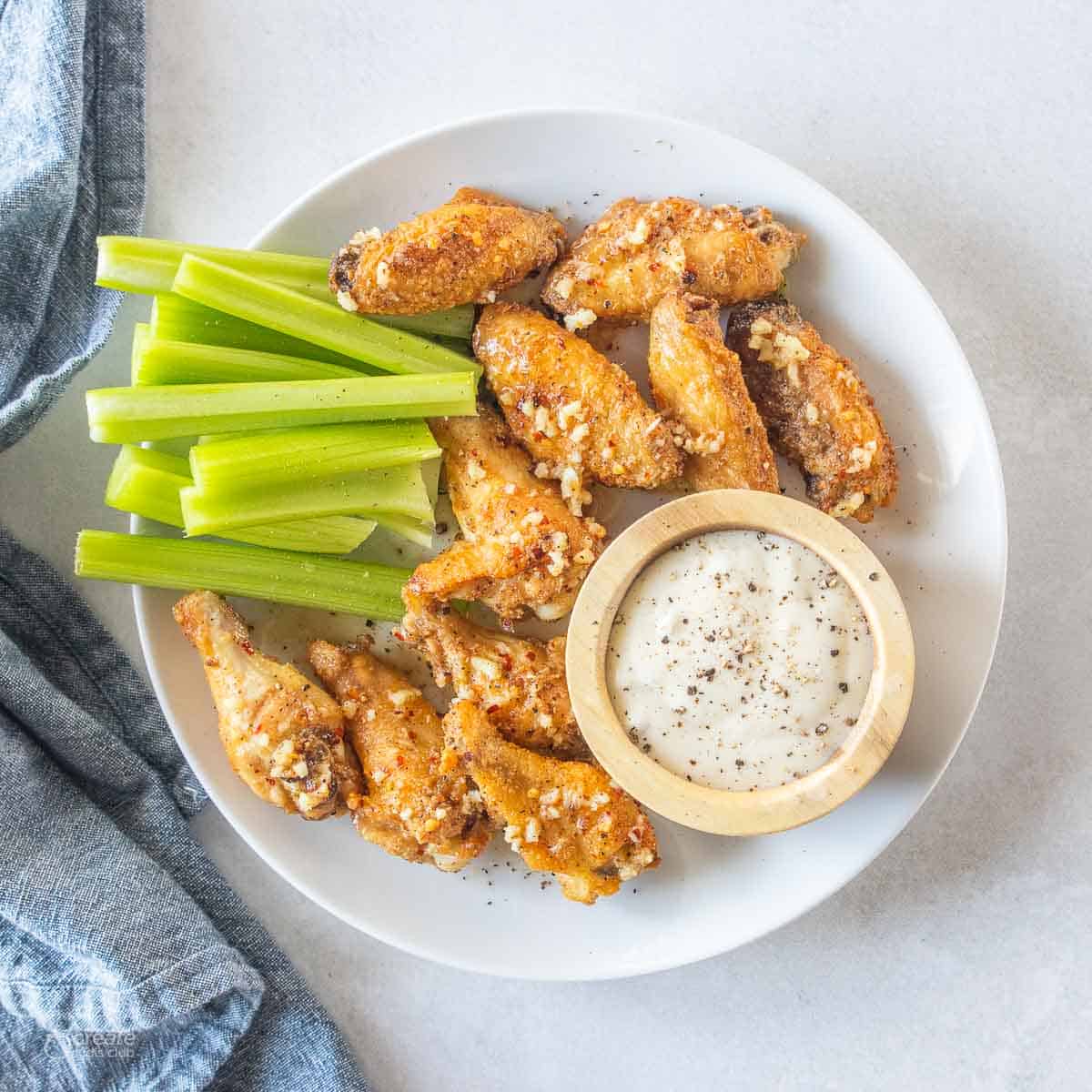 seasoned chicken wings on plate with celery sticks and dipping sauce