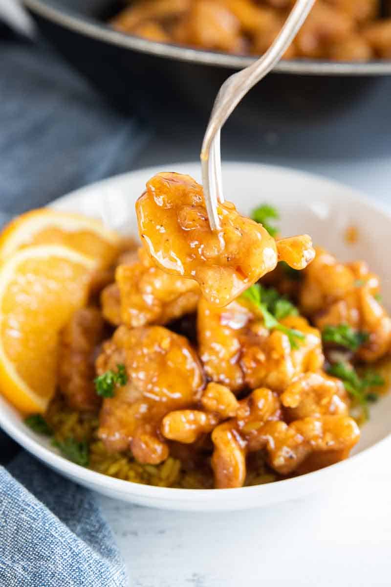 fork removing a piece of orange chicken from bowl