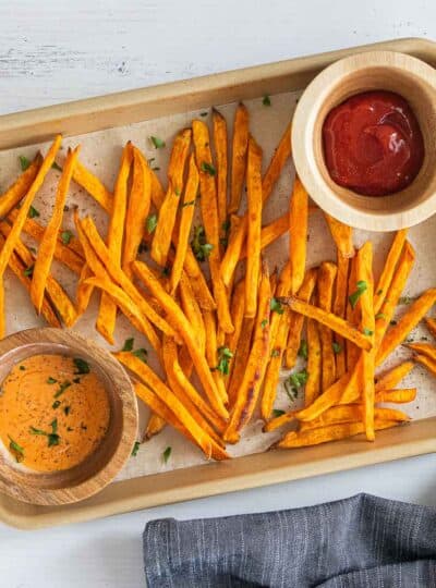 sweet potato fries on parchment lined baking sheet with gluten free dipping sauces