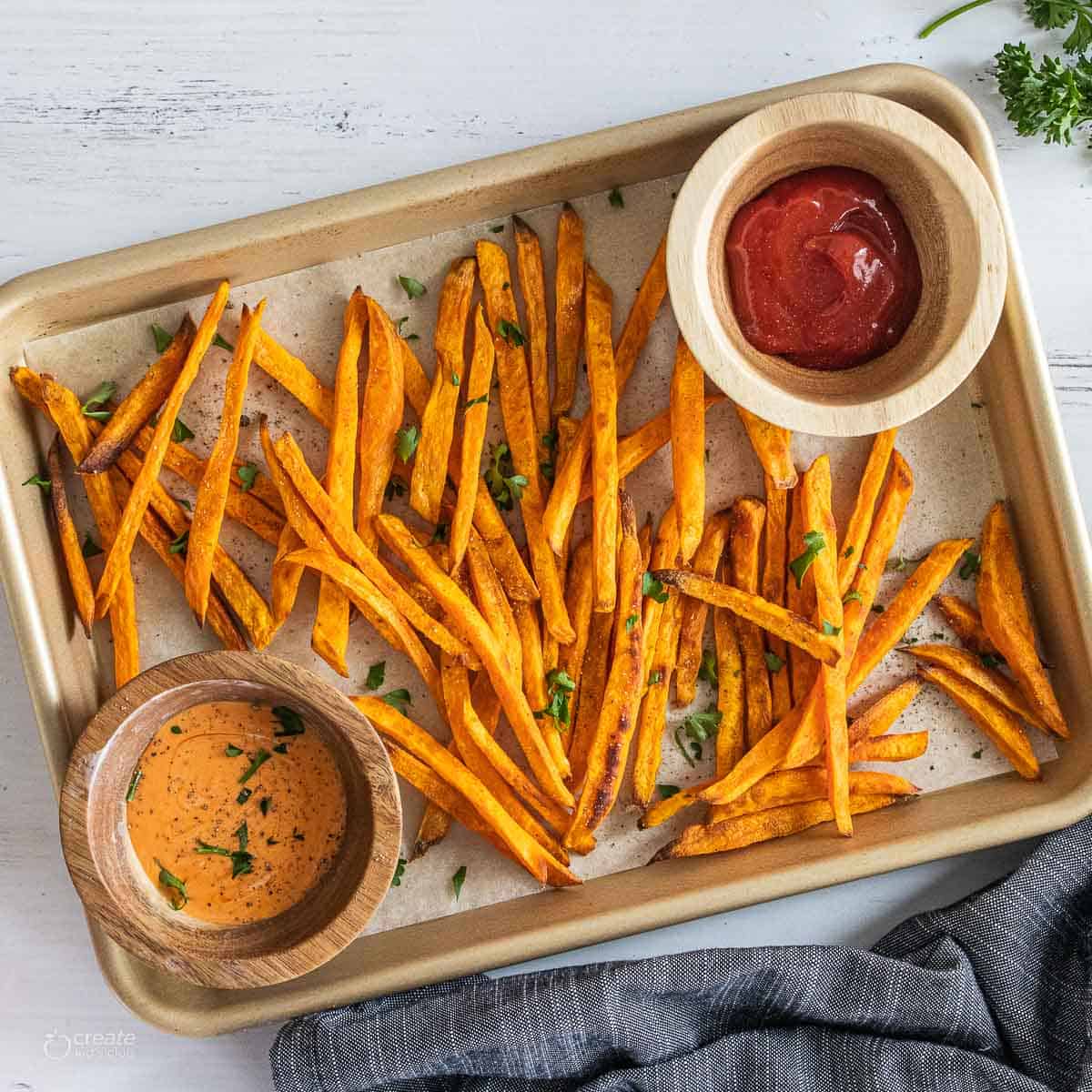 sweet potato fries on parchment lined baking sheet with gluten free dipping sauces