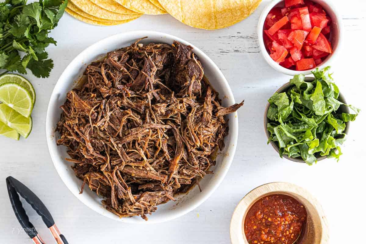 shredded roast in bowl next to taco toppings