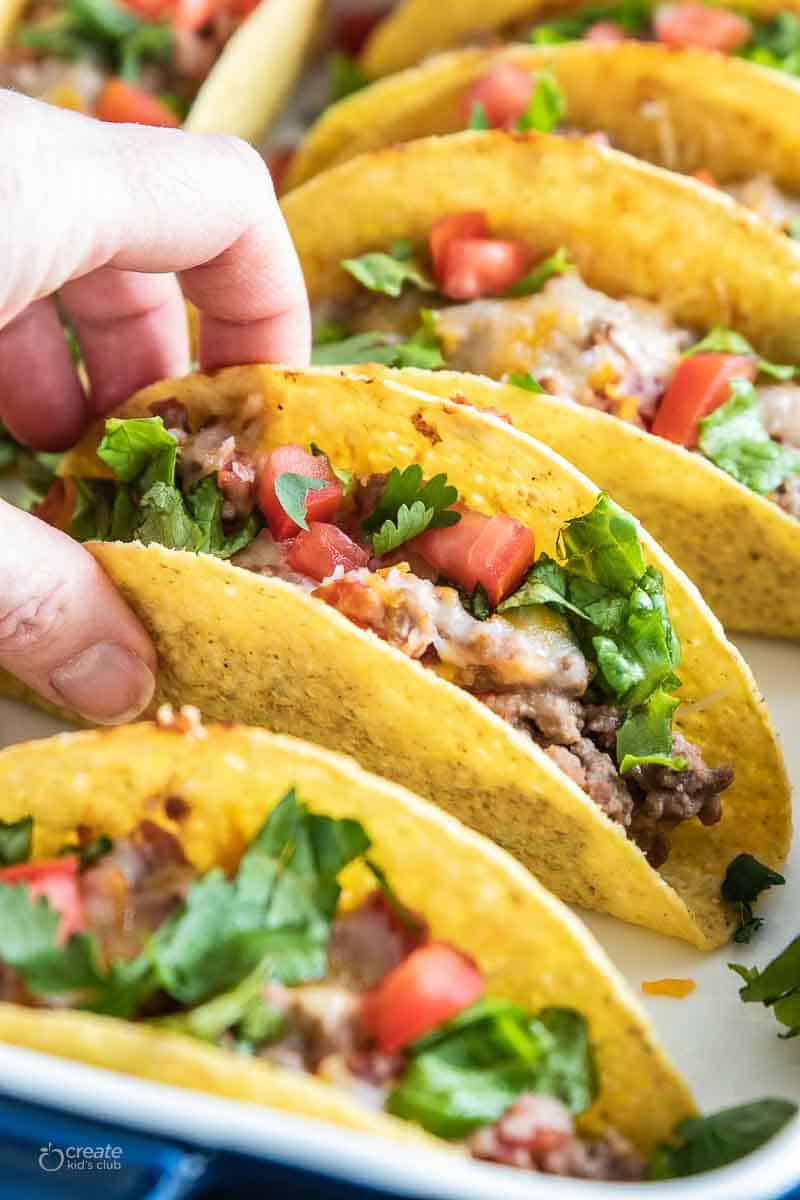 hand picking up a taco from baking dish