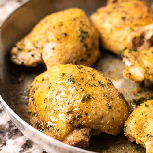 A close up of a baked chicken thigh shimmering with juices in a skillet.