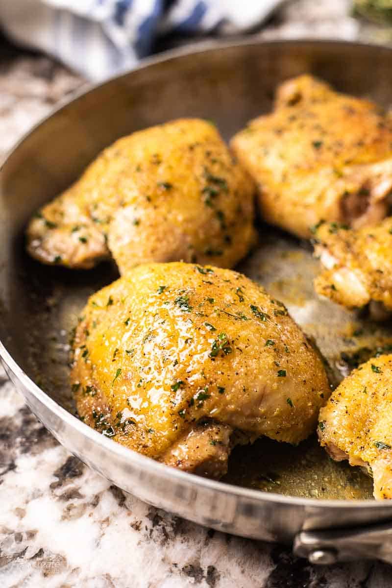 A close up of a baked chicken thigh shimmering with juices in a skillet.