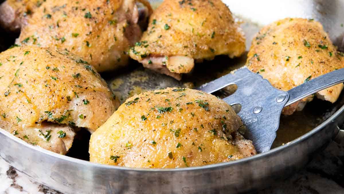 A close up of baked chicken thighs in a skillet with a flipper removing one.
