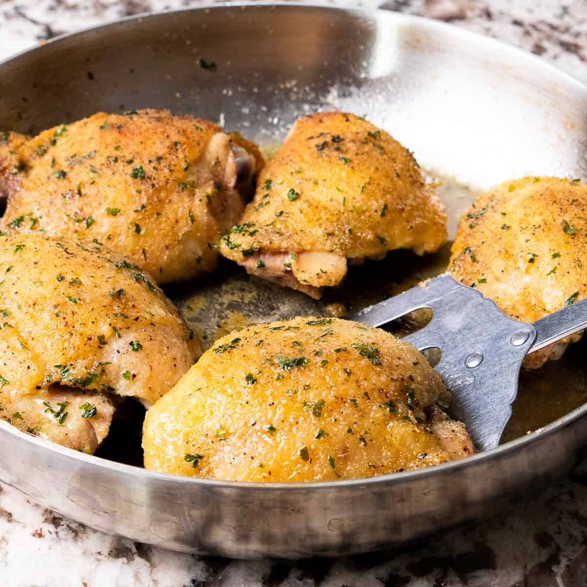 A close up of baked chicken thighs in a skillet with a spatula removing one.