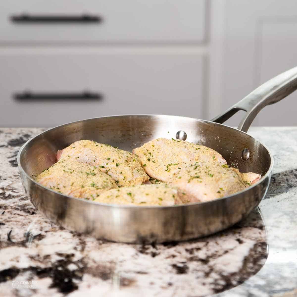 Uncooked, seasoned chicken thighs in a skillet.