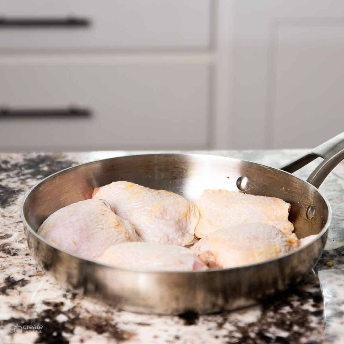 Raw chicken thighs in a skillet.