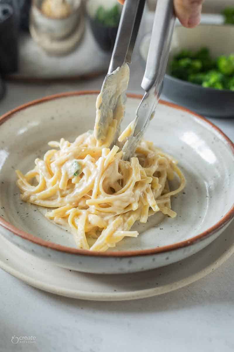 tongs placing serving of gluten free alfredo in bowl