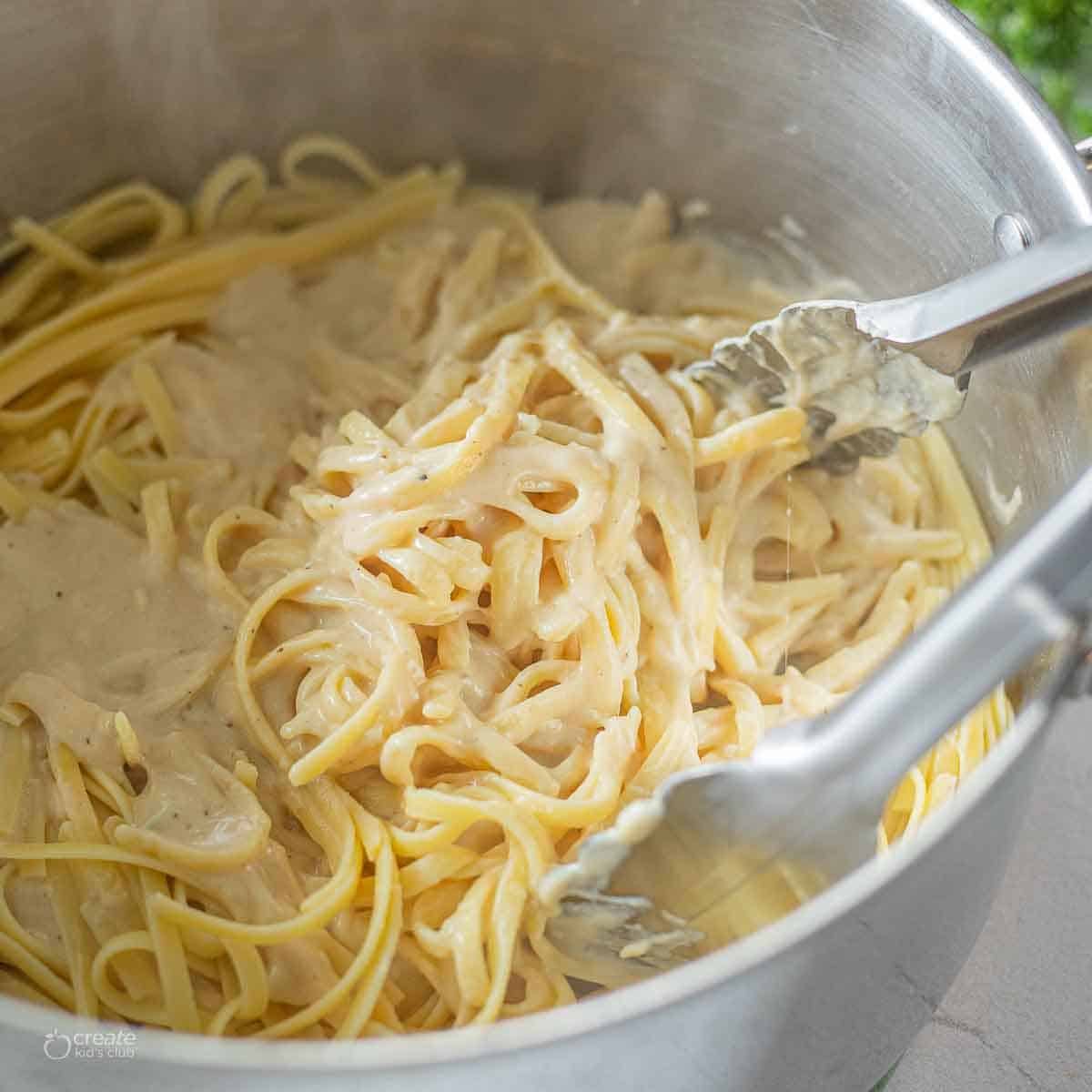 tongs stirring alfredo in pot