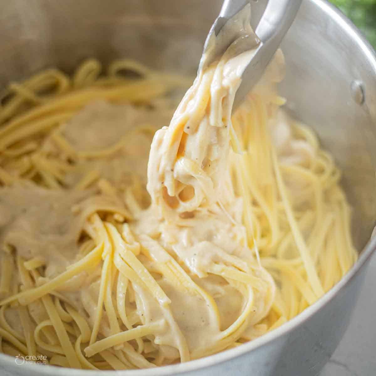 tongs stirring alfredo in pot