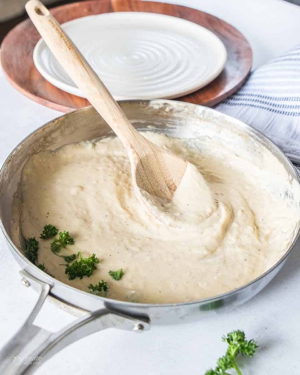 wooden spoon stirring alfredo sauce in pan
