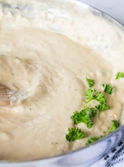 wooden spoon stirring alfredo sauce in pan