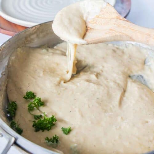 wooden spoon scooping gf alfredo sauce from pan