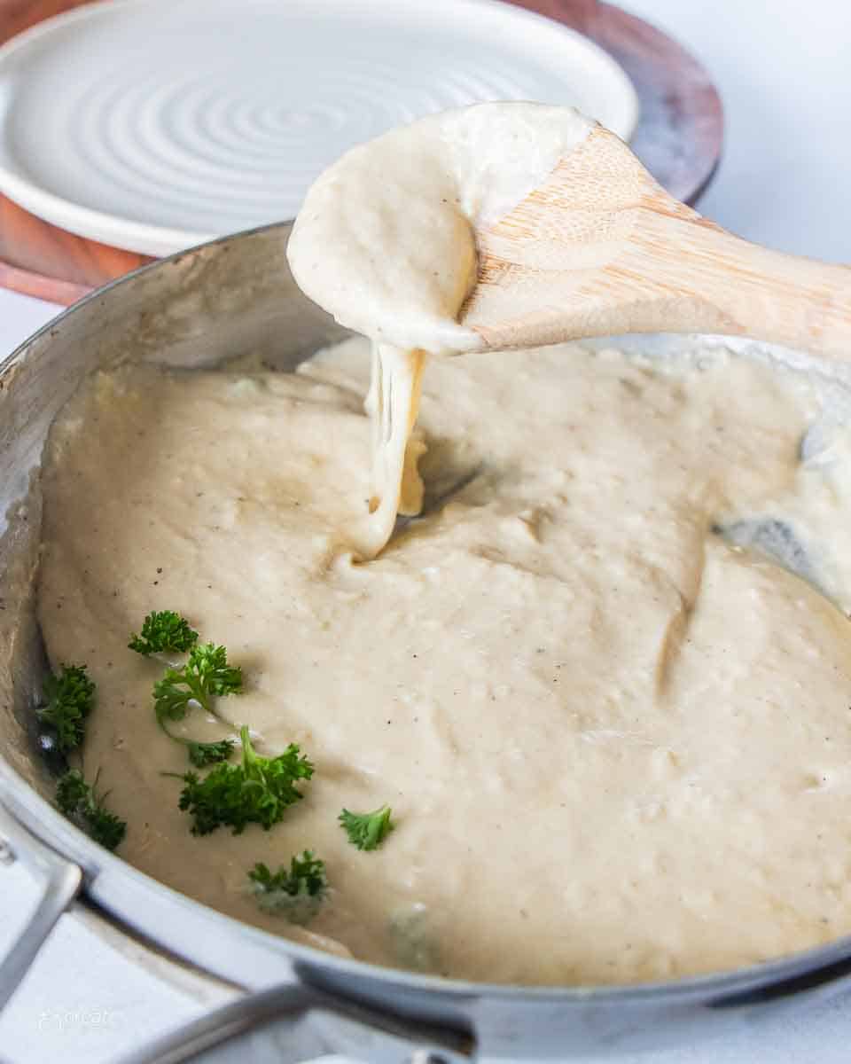 wooden spoon scooping gf alfredo sauce from pan