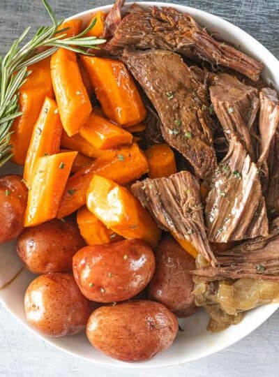 Roast beef with vegetables and gravy in a white bowl.