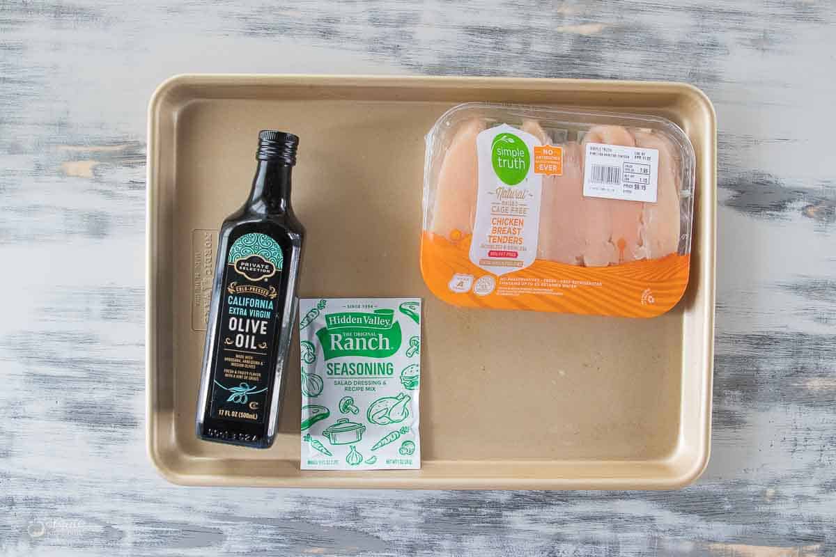 Chicken tenders in the packaging, dry ranch dressing and olive oil on a tray.