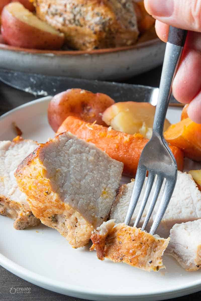 sliced pork roast on plate scooped by a fork
