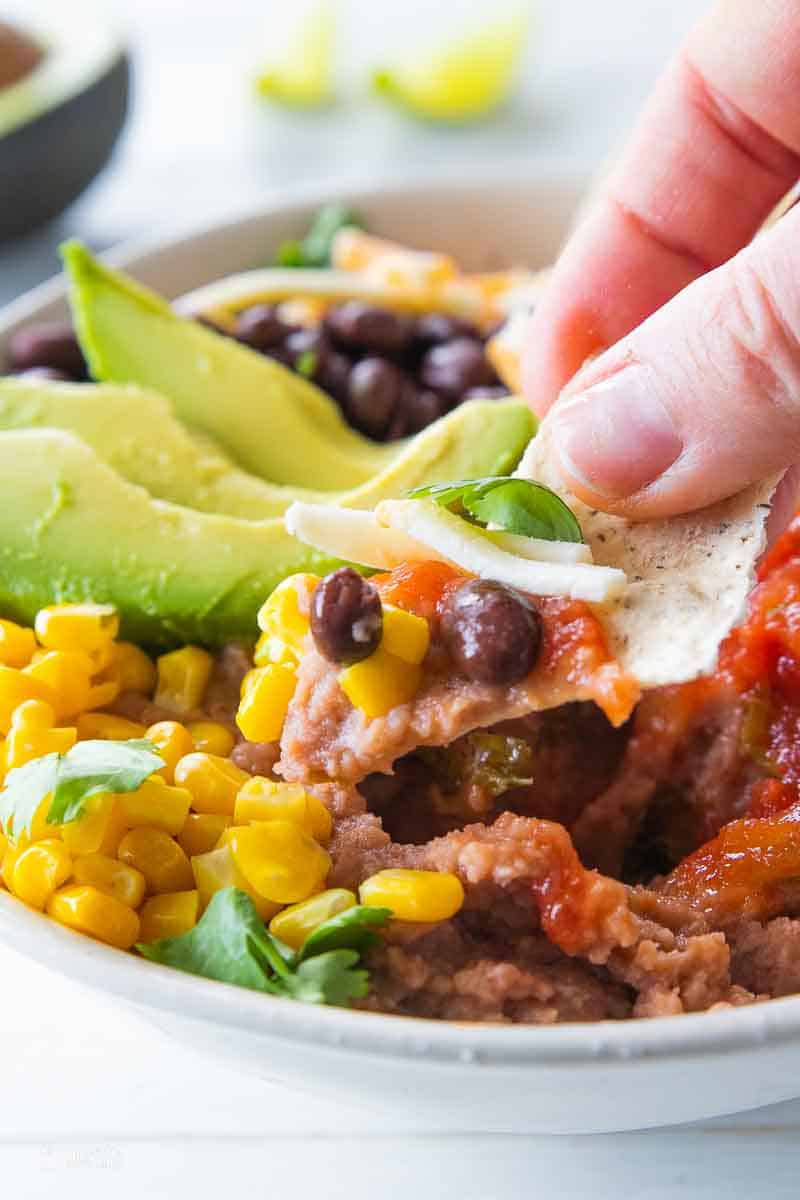 chip scooping ingredients in nacho bowl